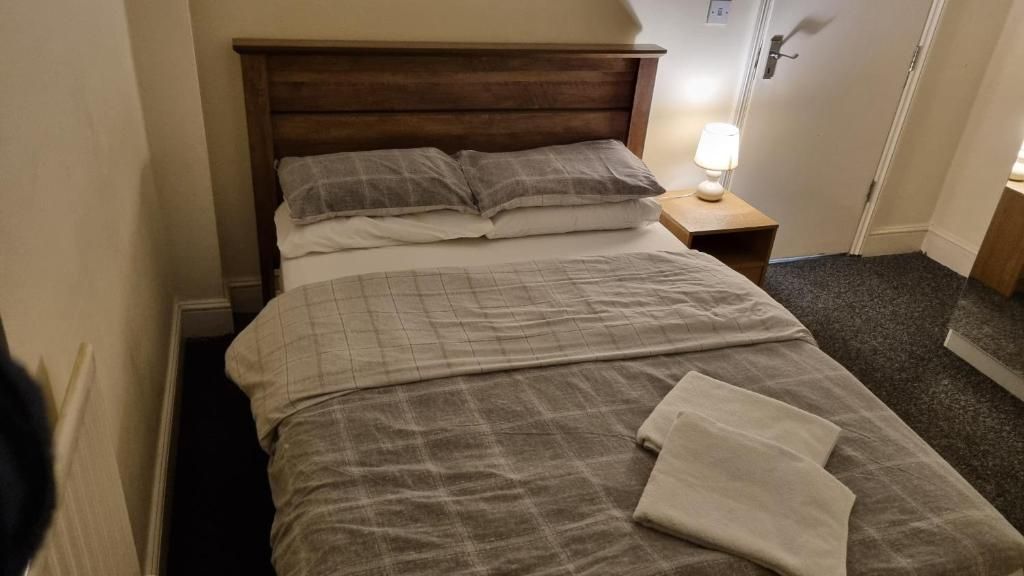 A hotel room with a wooden headboard, a bed with a checkered bedspread, two pillows, a bedside lamp, and a nightstand.