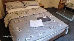 A neatly made bed with floral bedding, a bedside lamp, and a mirror on the wall. - Shamrock Guest House (Gravesend)