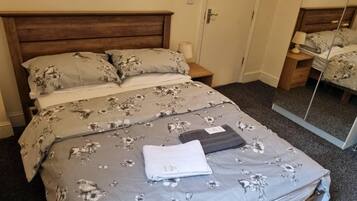 A neatly made bed with floral bedding, a bedside lamp, and a mirror on the wall.