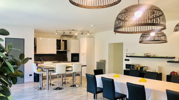 A modern kitchen with white cabinets, a central island, and a dining area with a white table and black chairs. - Guest house 296 (Verona)