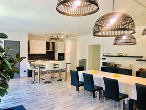 A modern kitchen with white cabinets, a central island, and a dining area with a white table and black chairs. - Guest house 296 (Verona)