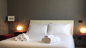 A large bed with white linens and rolled towels, a headboard, and bedside lamps. - Guest house 296 (Verona)