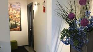 A hallway with a large floral arrangement, a painting of a cityscape, and a door with a light switch. - Guest house 296 (Verona)