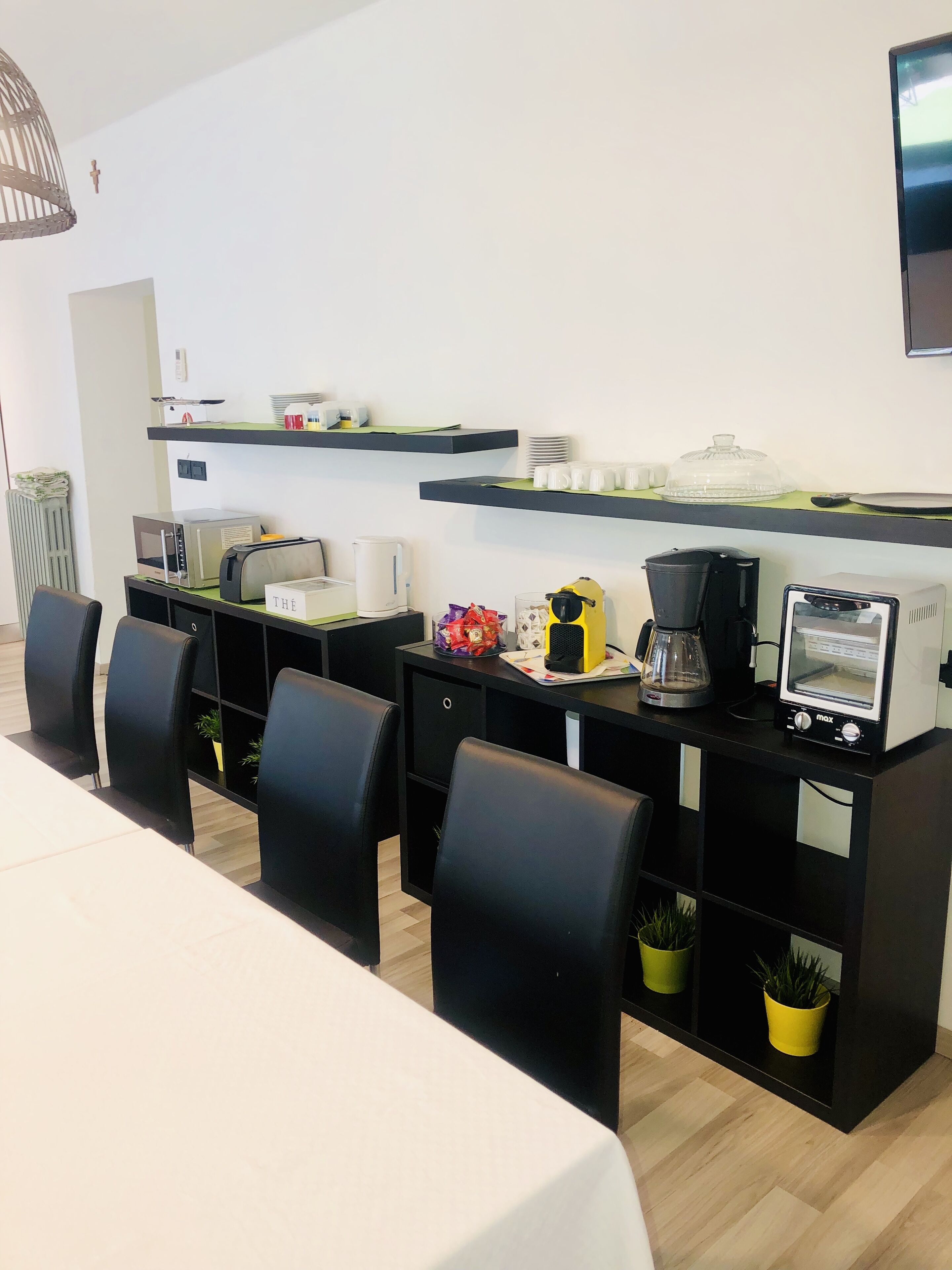 A modern hotel room with a dining area, a kitchenette, and a flat-screen TV mounted on the wall.