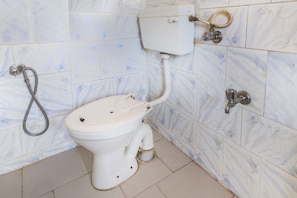 A toilet with a bidet attachment, a handheld showerhead, and a wall-mounted faucet.