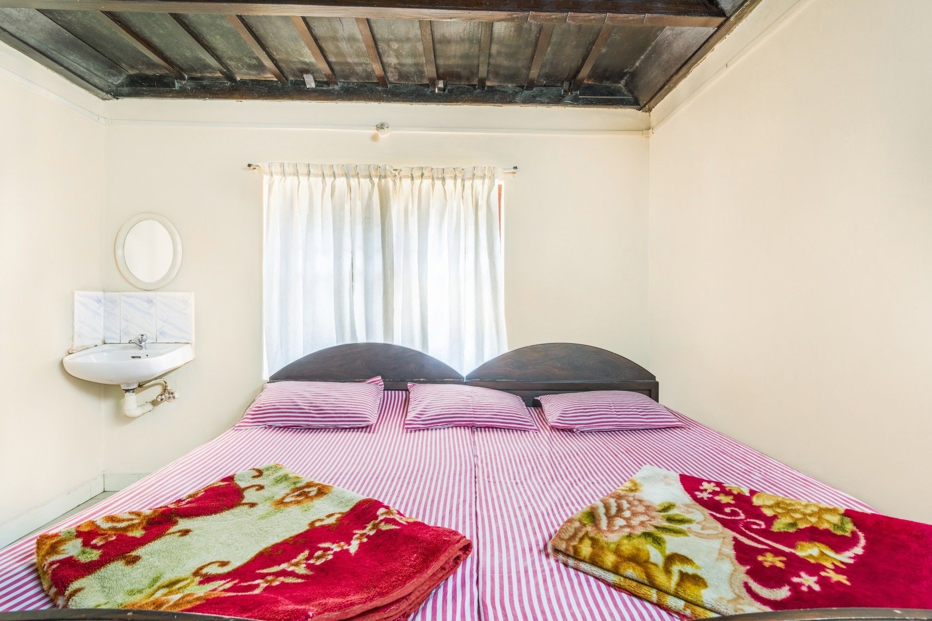 A bedroom with a bed, two pillows, a bedside table, a mirror, and a window with curtains.