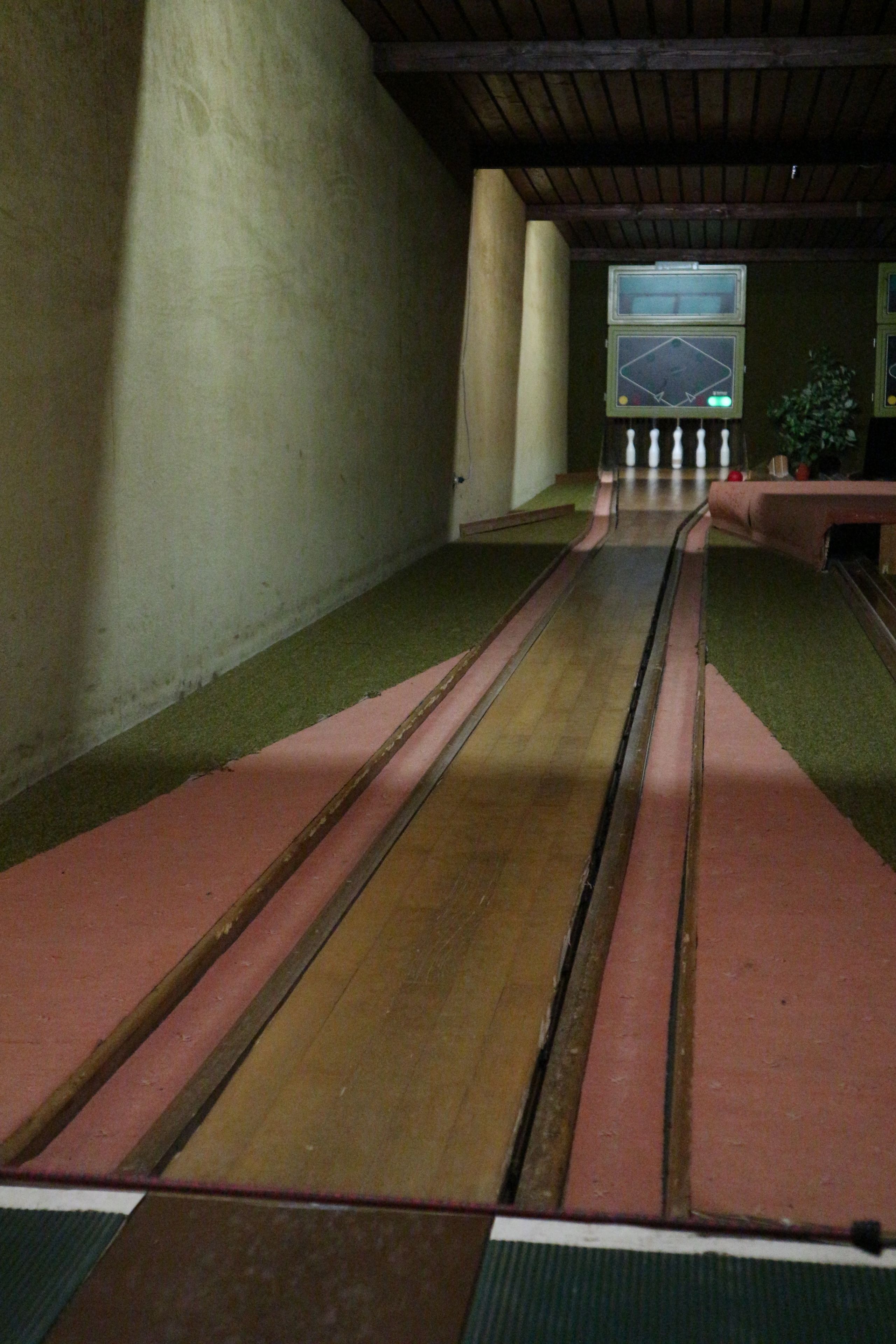 A bowling alley with lanes marked in red and green, wooden floor, and a scoreboard in the background.