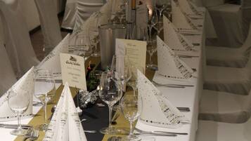 A formal dining room with a long table set for a meal, white chairs, and candles.