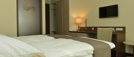 A hotel room with a bed, a desk, a chair, a TV, and a mirror.