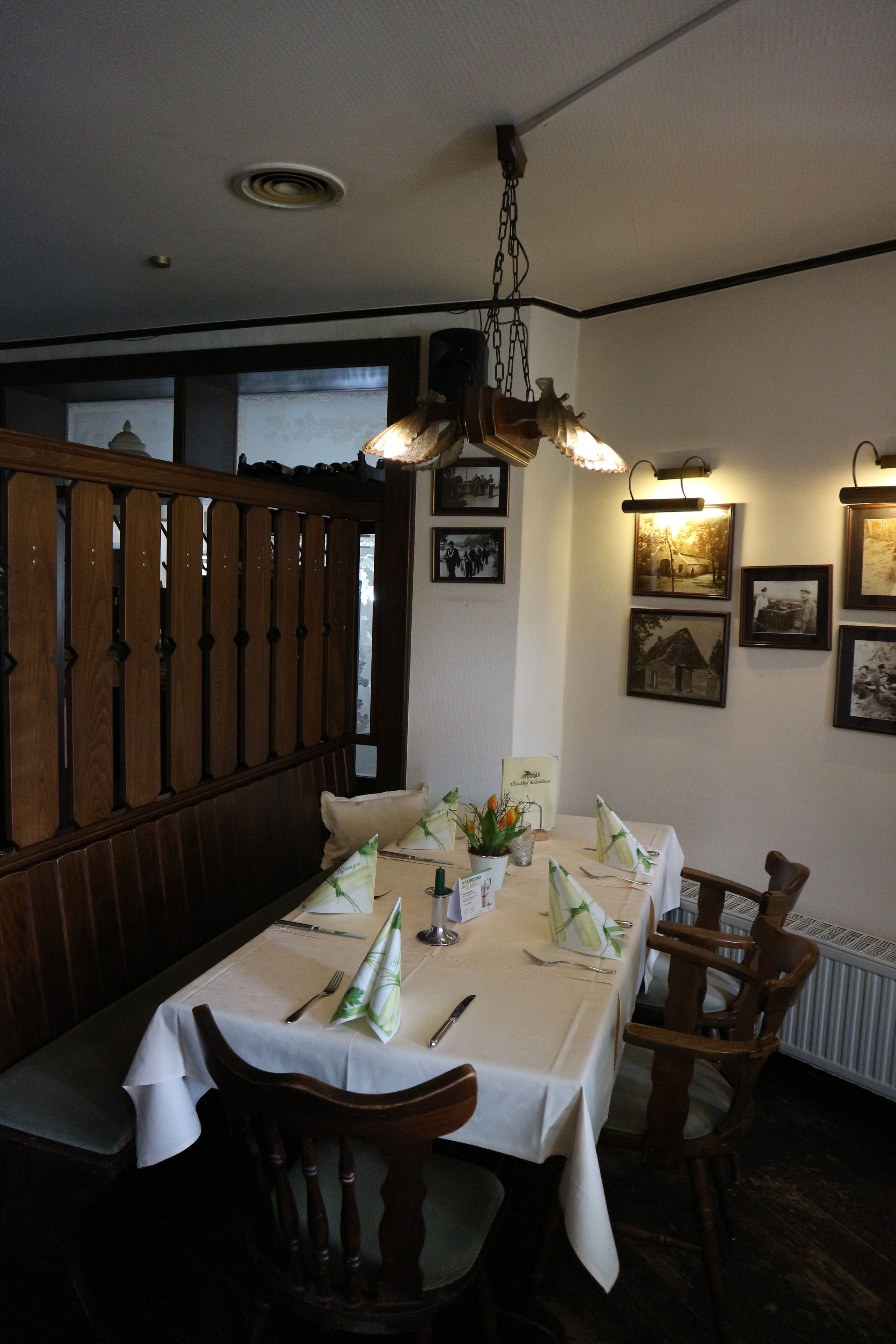 Un comedor con una mesa dispuesta para cuatro, sillas de madera, una lámpara colgante y cuadros en la pared.