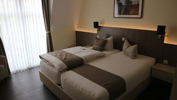 Ein modernes Hotelzimmer mit einem großen Bett, Nachttischen, einem Sessel und einem Fenster mit Vorhängen.