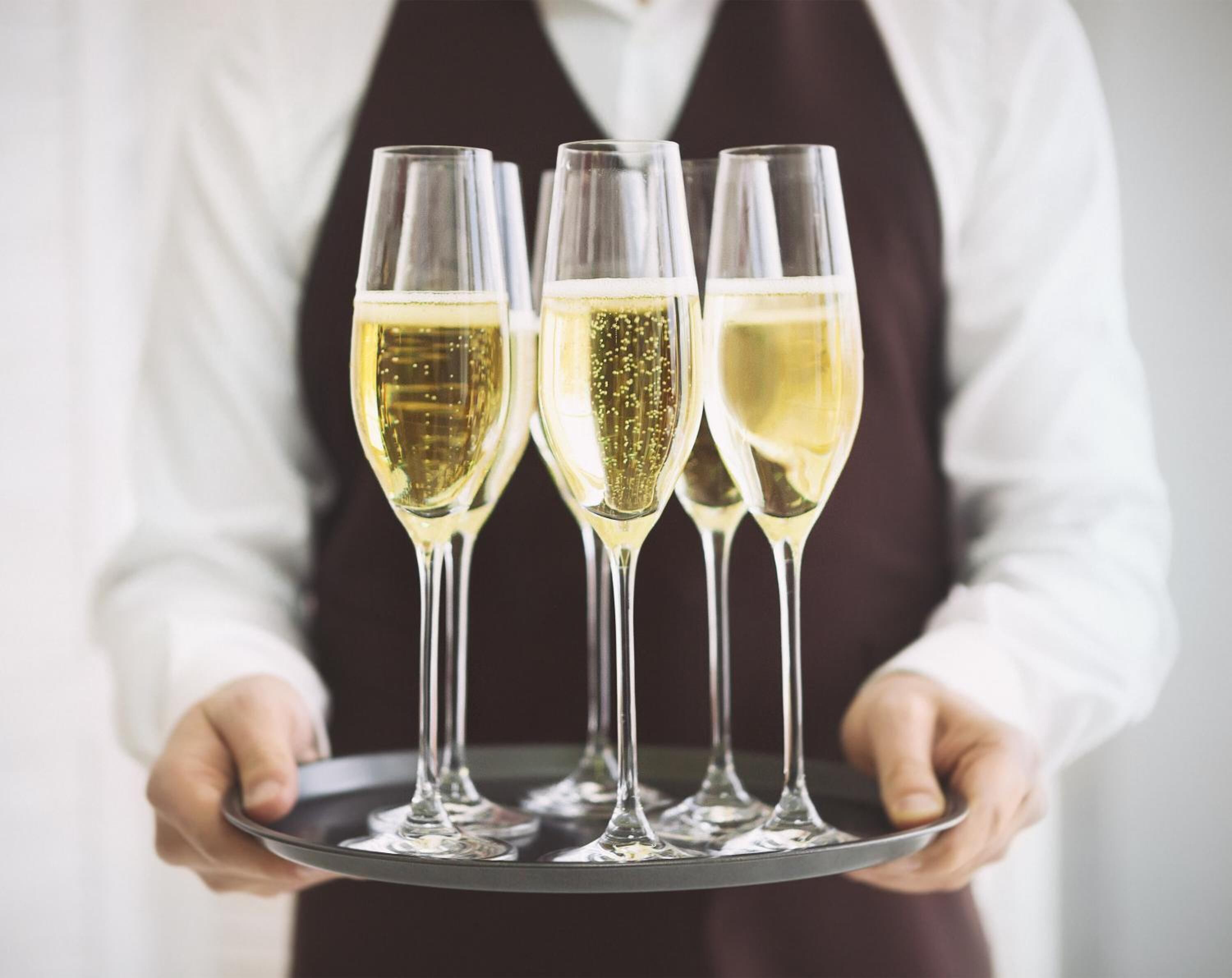 Iemand houdt een dienblad vast met daop drie champagneglazen.