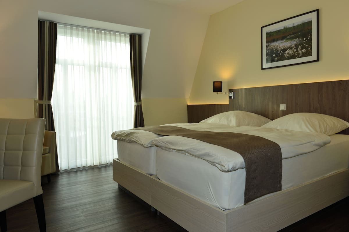 A hotel room with a large bed, a chair, a window with curtains, and a framed picture on the wall.