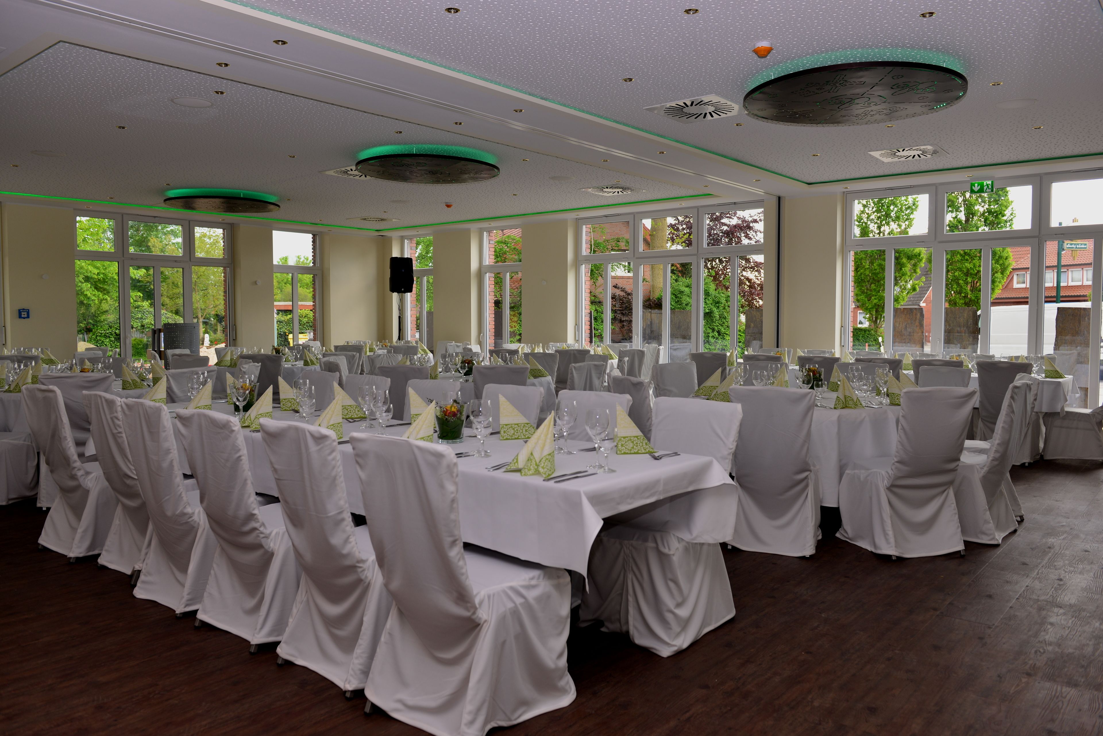 Un salón de banquetes con varias mesas redondas, manteles blancos y sillas con fundas blancas.