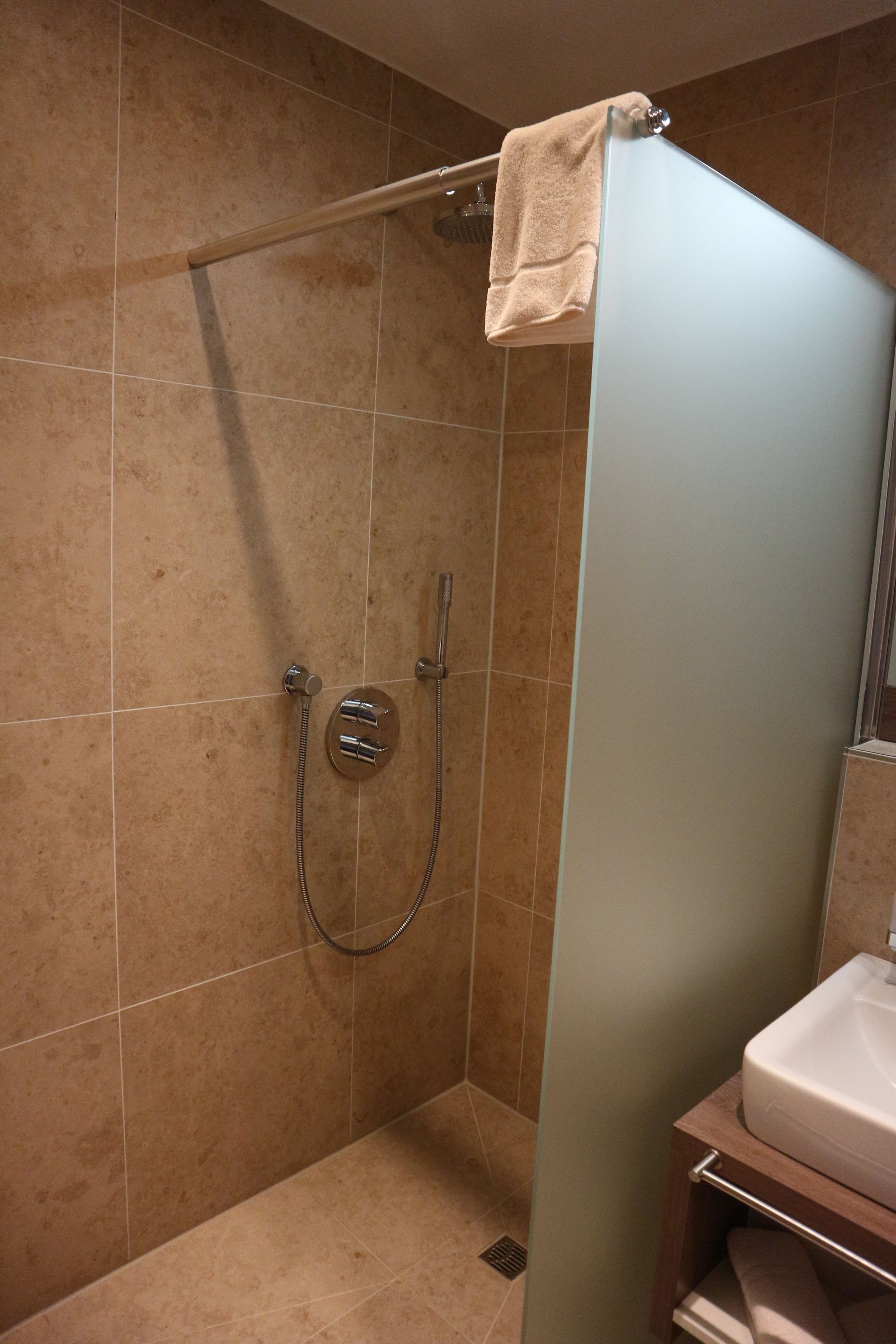 A modern bathroom with a glass shower enclosure, a handheld showerhead, and a towel rack.