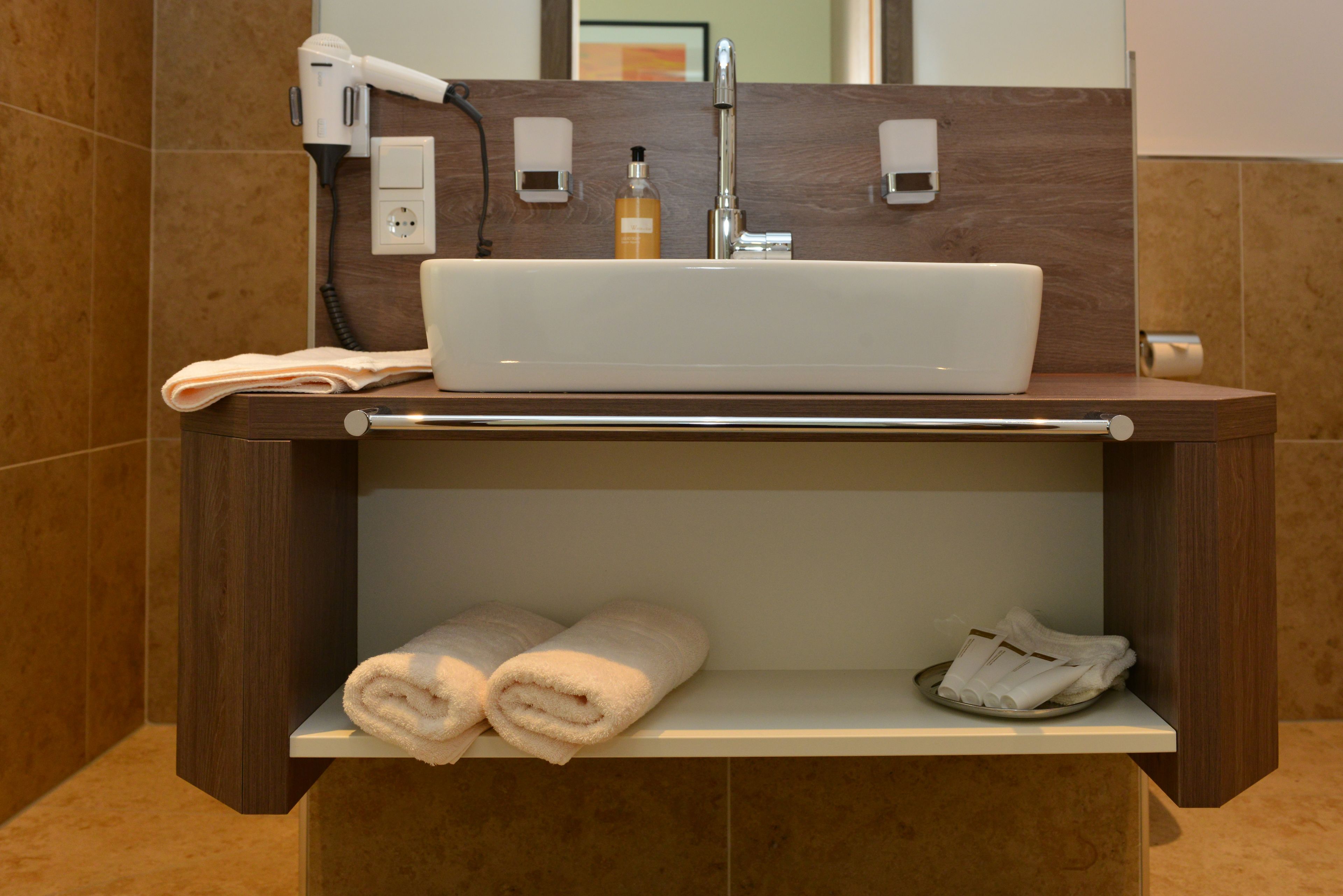A bathroom with a white sink, a hair dryer, a bottle of soap, and neatly folded towels.