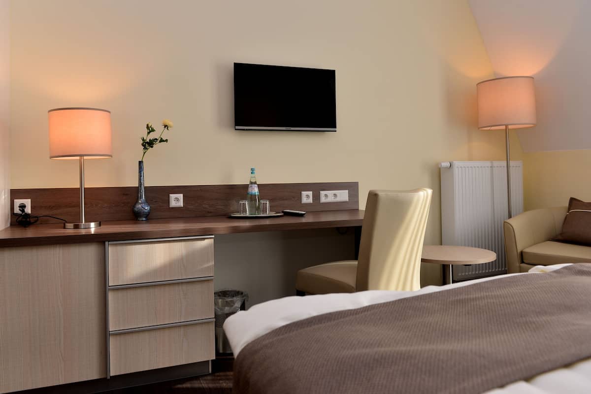 A hotel room with a bed, a desk with a lamp, a TV, and a chair.