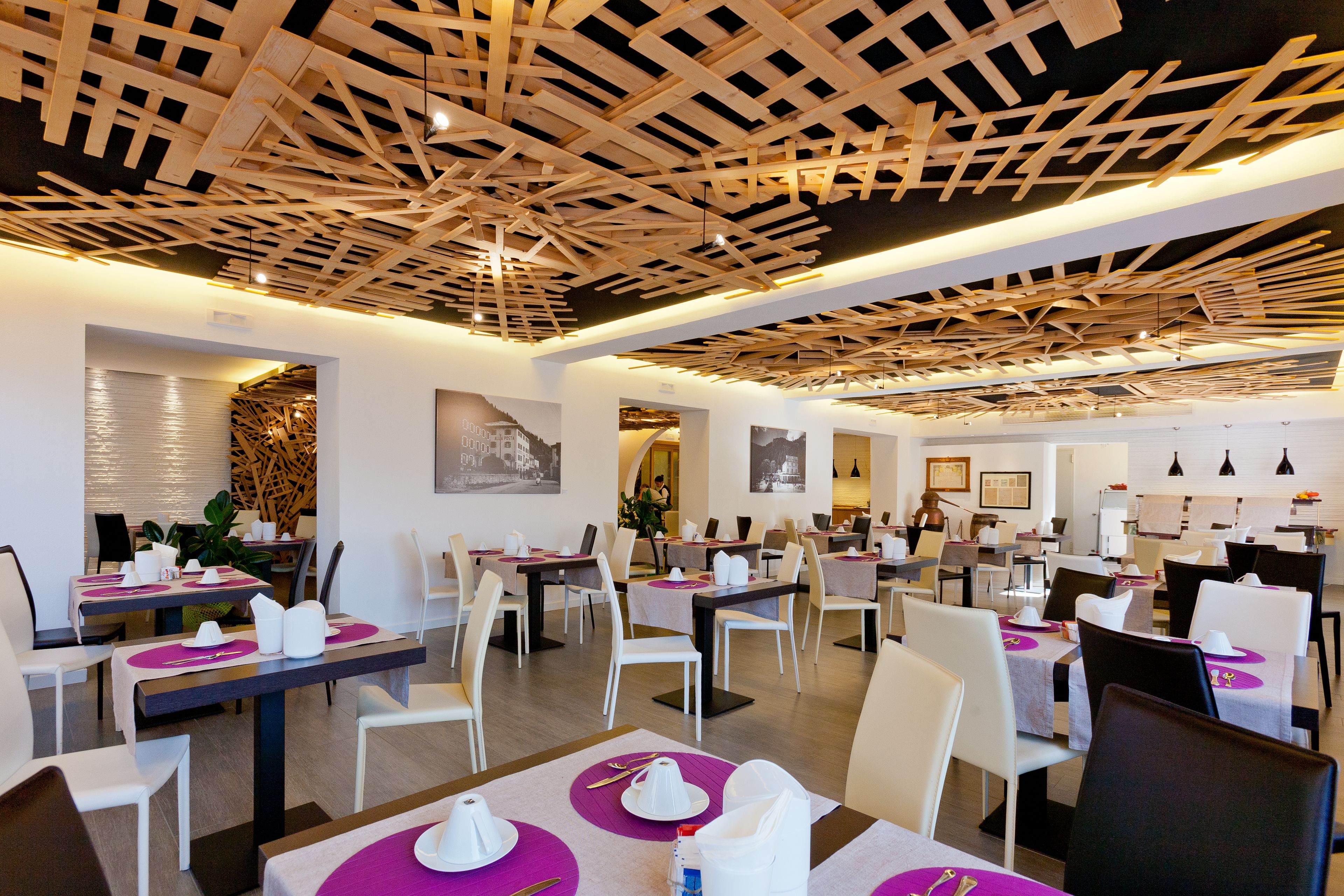 A modern restaurant with white and dark wooden tables, purple placemats, and a unique ceiling design.