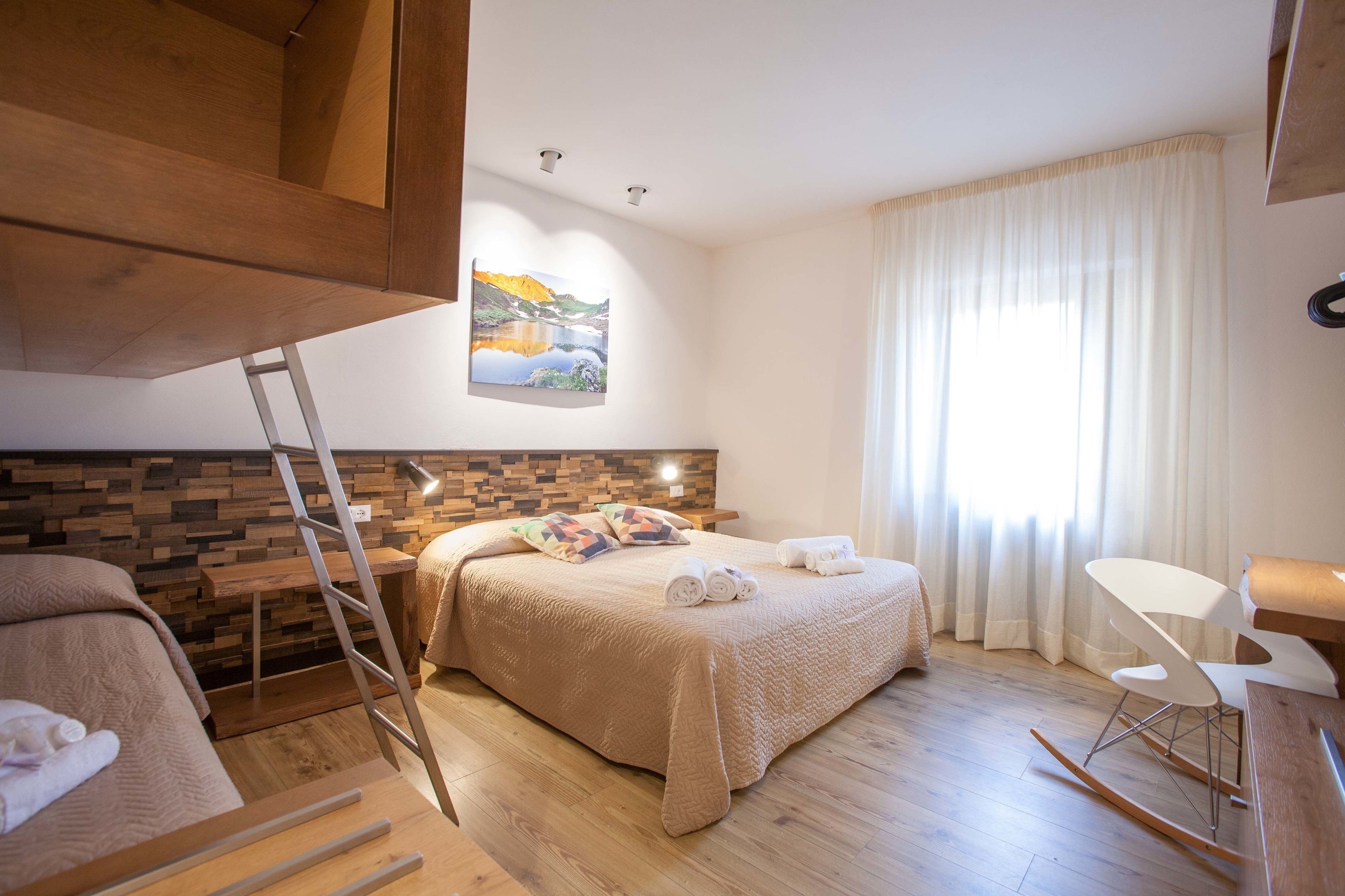 A bedroom with a wooden headboard, a bed with a quilt, a ladder, a desk, and a chair.
