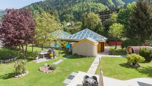 A hotel with a glass-roofed building, a stone patio, and a view of a forested mountain. - Grand Hotel Gortani Wellness & Relax (Arta Terme)