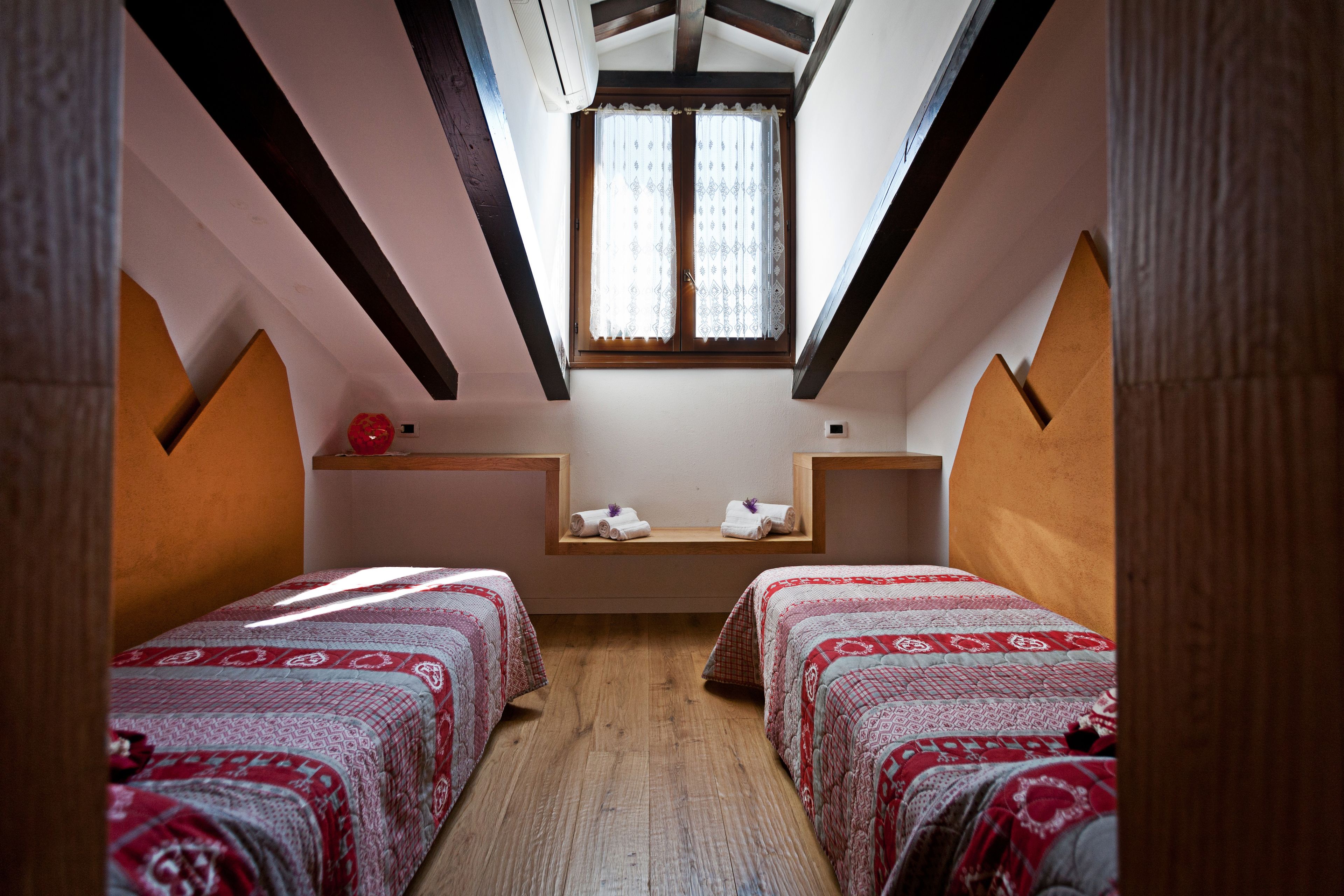 Een knus kamertje met twee bedden, een raam met gordijnen en een houten plafond.