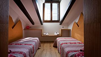 Een knus kamertje met twee bedden, een raam met gordijnen en een houten plafond.