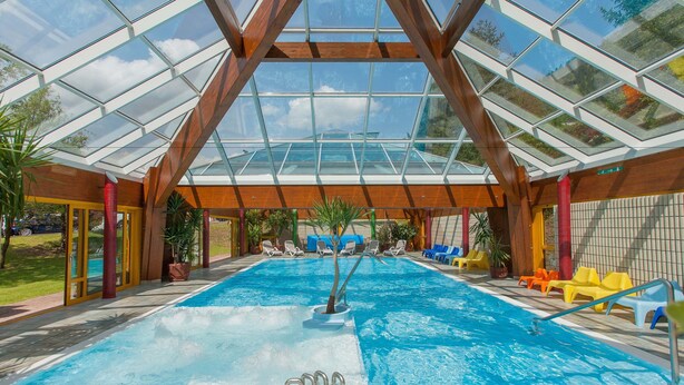 An indoor swimming pool with a glass ceiling, wooden beams, and colorful lounge chairs. - Grand Hotel Gortani Wellness & Relax (Arta Terme)