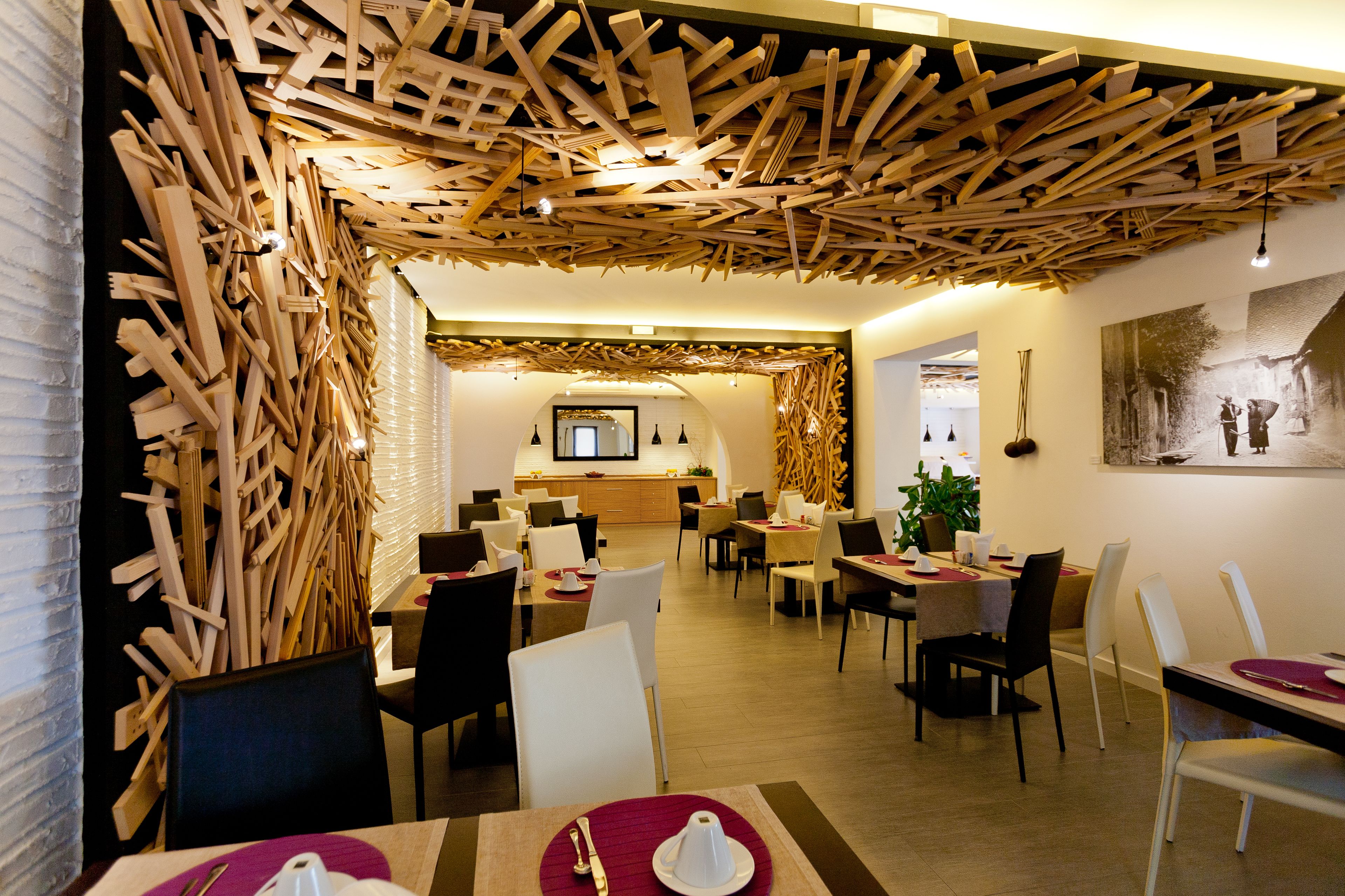 Un espace de restauration moderne avec des panneaux de plafond en bois, des tables recouvertes de nappes blanches et agrémentées de sets de table rouges, et un grand tableau accroché au mur.
