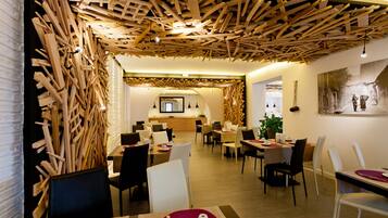 Un espace de restauration moderne avec des panneaux de plafond en bois, des tables recouvertes de nappes blanches et agrémentées de sets de table rouges, et un grand tableau accroché au mur.