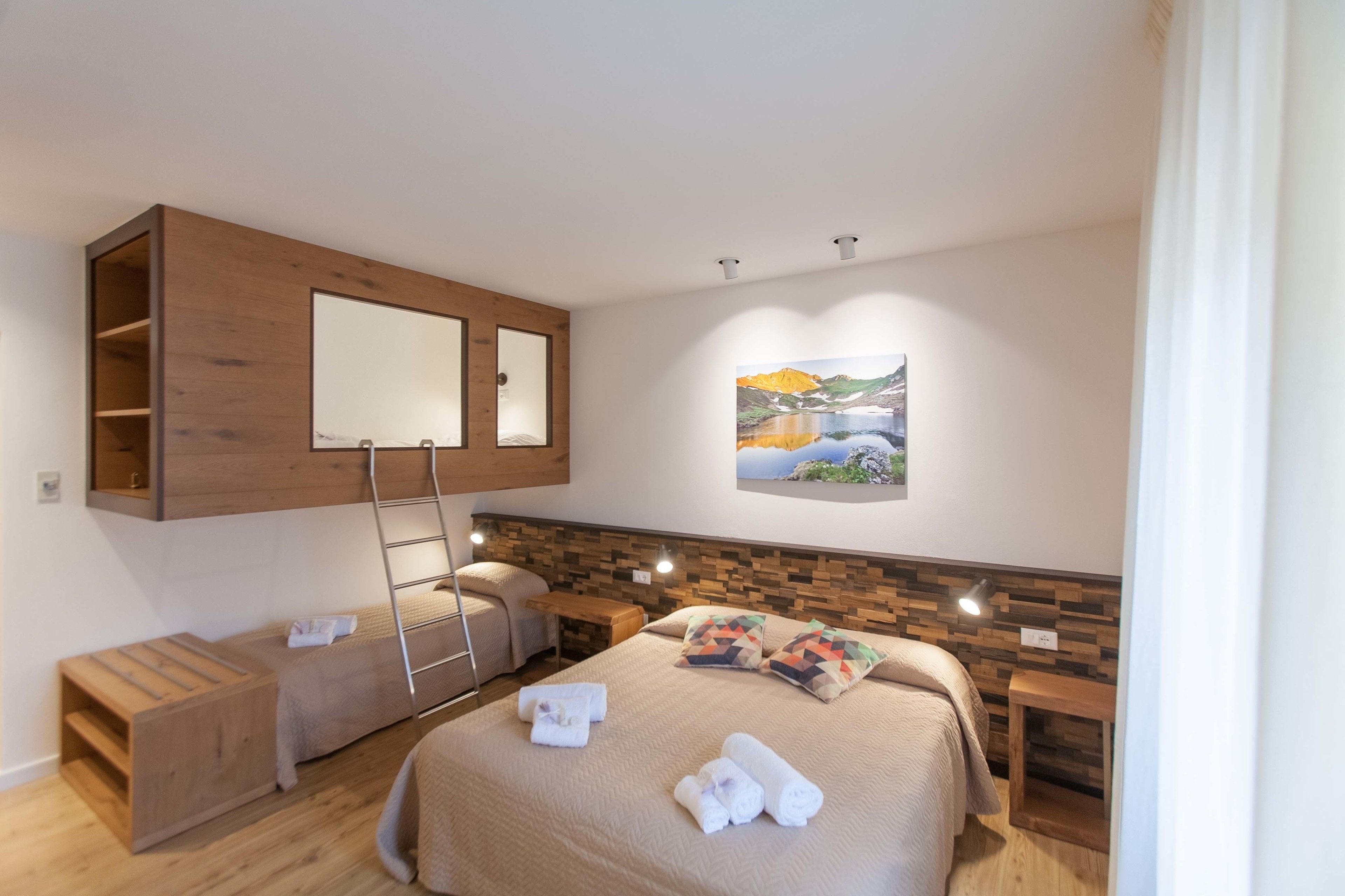 A modern hotel room with a bunk bed, a wooden headboard, a painting, and a small wooden table.