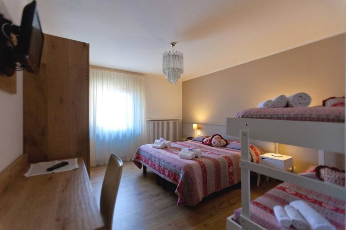 Une chambre avec un lit superposé, un bureau, une chaise, un lustre et une fenêtre avec des rideaux.