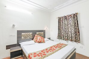 A hotel room with a bed, a nightstand, a wall-mounted lamp, and a window with patterned curtains.