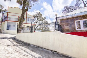 A concrete wall with a metal railing, a building with a red roof, and a tree in the background. - GuestHouser 1 BR Boutique stay 5a75 (Dalhousie)