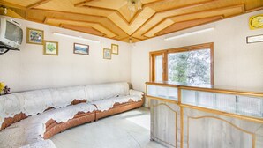 Ein gemütliches Zimmer mit Holzbalkendecke, einem Sofa mit Spitzenüberwurf, einem kleinen Tisch und gerahmten Bildern an der Wand.
