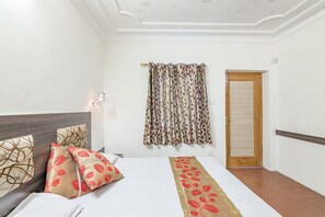 A hotel room with a bed, a headboard, a wall-mounted lamp, a patterned curtain, and a wooden door. - GuestHouser 1 BR Boutique stay 5a75 (Dalhousie)