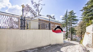 Eine Betonmauer mit einem Metallgitter, einem roten und schwarzen Bogen und einem Feldweg, der zu einem Gebäude mit einem Metalldach führt.