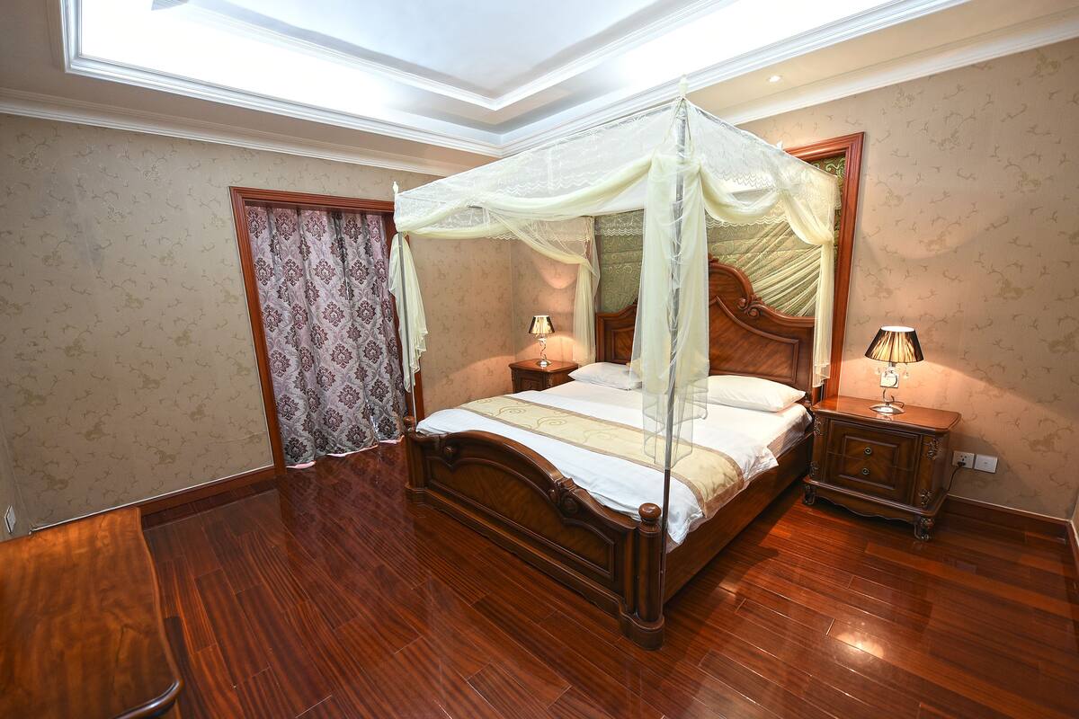 A bedroom with a four-poster bed, wooden flooring, a nightstand, and a bedside table with lamps.