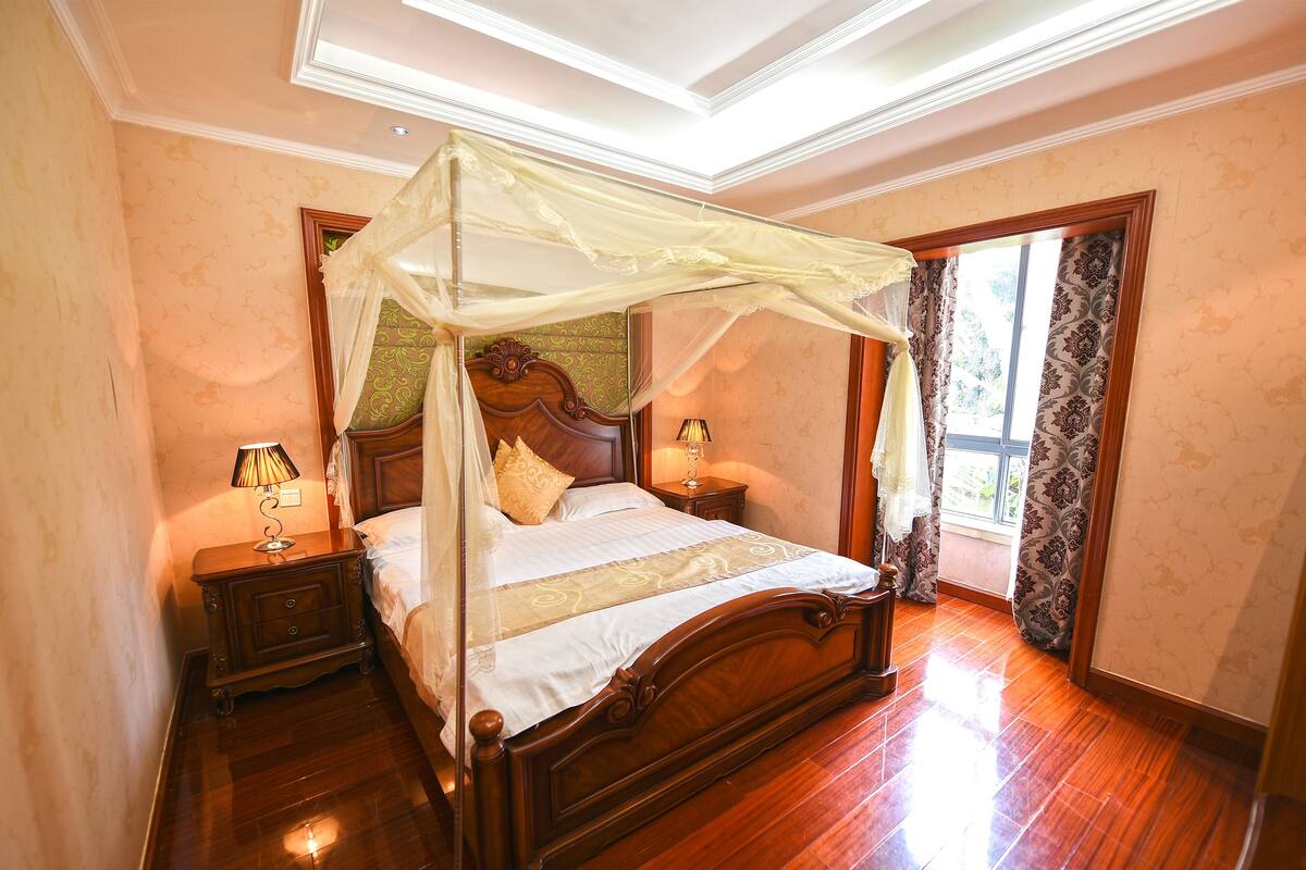 A bedroom with a four-poster bed, wooden headboard, bedside tables with lamps, and a window with patterned curtains.