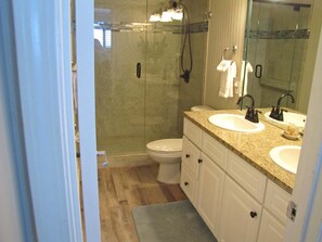 A bathroom with a glass-enclosed shower, a white toilet, and a vanity with two sinks. - Beach House Condos by Crystal Waters (Destin)