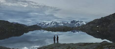 A lake surrounded by mountains with two people standing on a rocky shore.