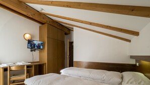 A bedroom with a bed, wooden headboard, a TV mounted on the wall, and a wooden wardrobe. - Hotel Ferrari (Pinzolo)