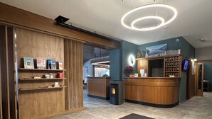 A modern reception area with a wooden reception desk, a black carpet, and a large circular light fixture on the ceiling. - Hotel Ferrari (Pinzolo)