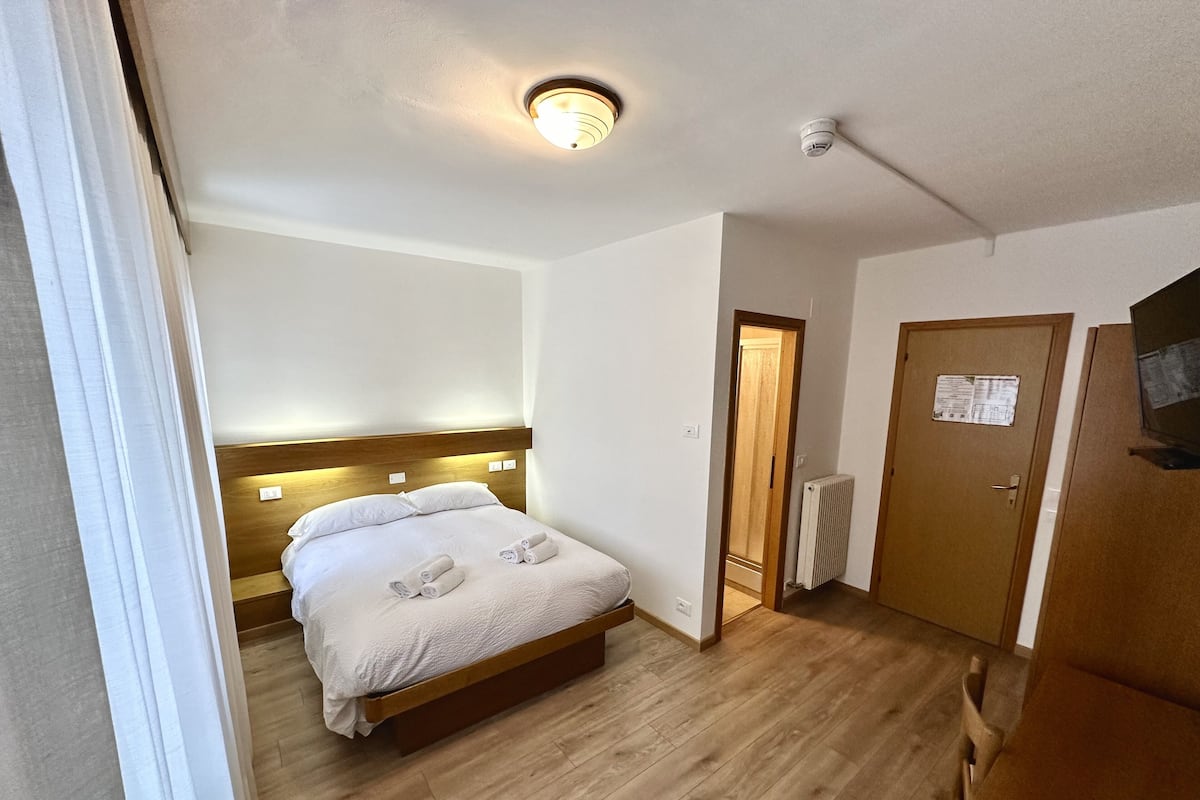 Hotellihuone, jossa on puinen sänky, kattovalaisin, patteri ja ovi, jossa on lappu.