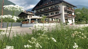 A multi-story hotel with balconies adorned with flowers, surrounded by lush greenery and mountains. - Hotel Ferrari (Pinzolo)