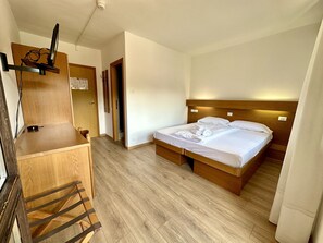 A hotel room with a wooden desk, a bed with white linens, and a wooden headboard.