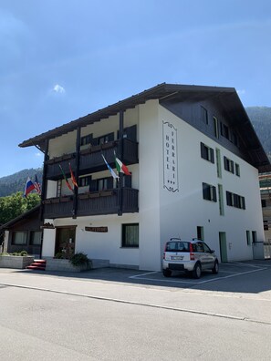 A two-story hotel with balconies, a sign reading "Hotel Ferrari", and flags of Italy, Russia, and another country.