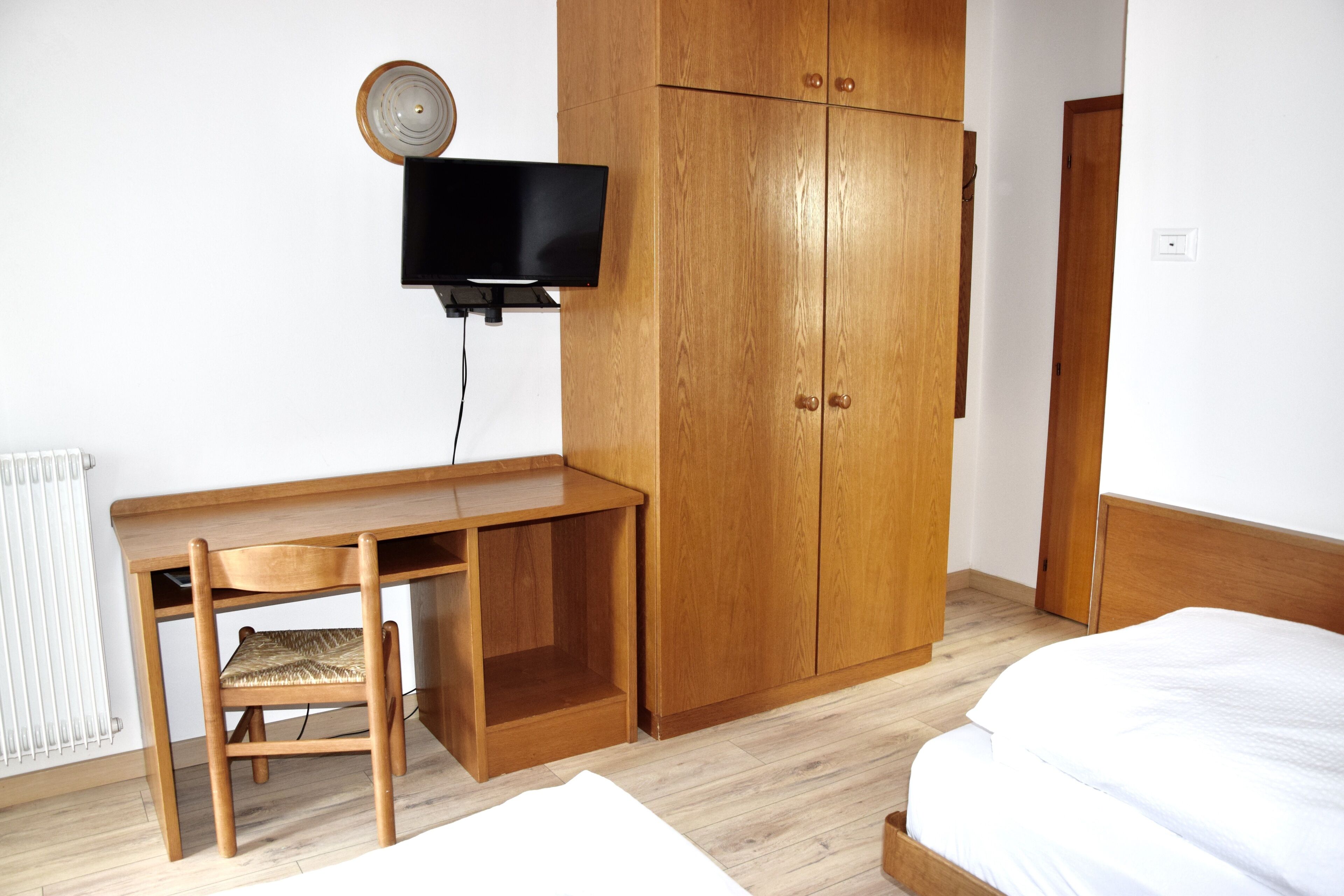 Ein Zimmer mit Holzschreibtisch, einem an der Wand montierten Fernseher, einem Kleiderschrank und einem Bett.