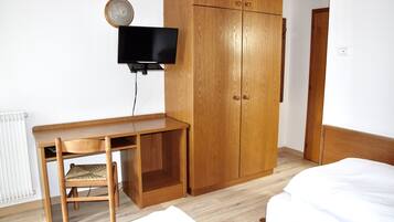 Ein Zimmer mit Holzschreibtisch, einem an der Wand montierten Fernseher, einem Kleiderschrank und einem Bett.