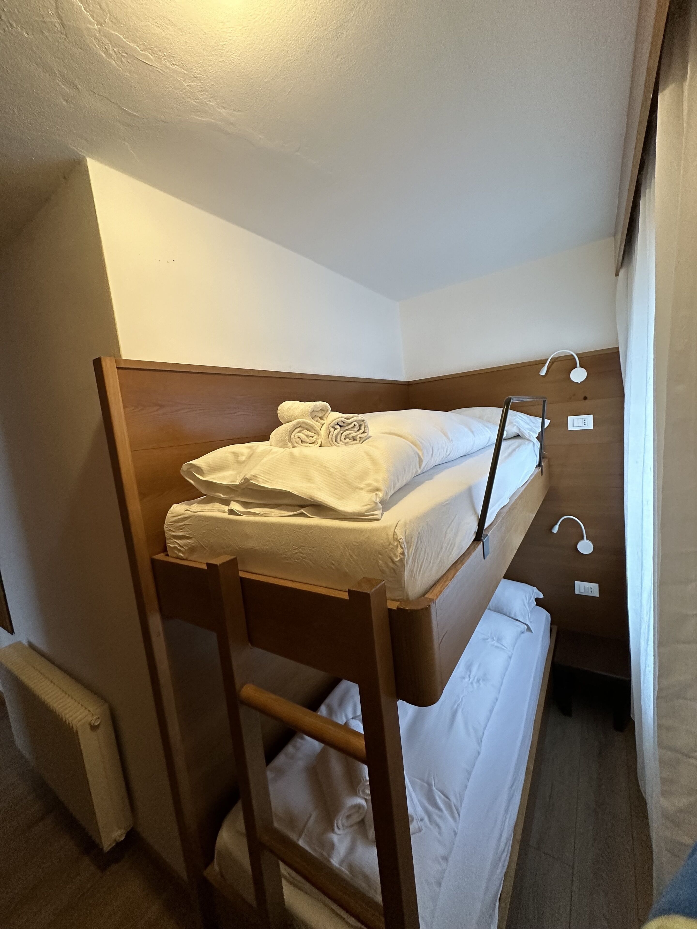 Un letto a castello con struttura in legno e biancheria bianca, una scala e un piccolo comodino con una lampada.
