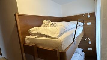 Un letto a castello con struttura in legno e biancheria bianca, una scala e un piccolo comodino con una lampada.